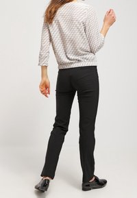 Pull en motif gris clair avec des manches trois quarts, associé à un pantalon noir ajusté et des chaussures noires. Texture lisse, coupe décontractée.