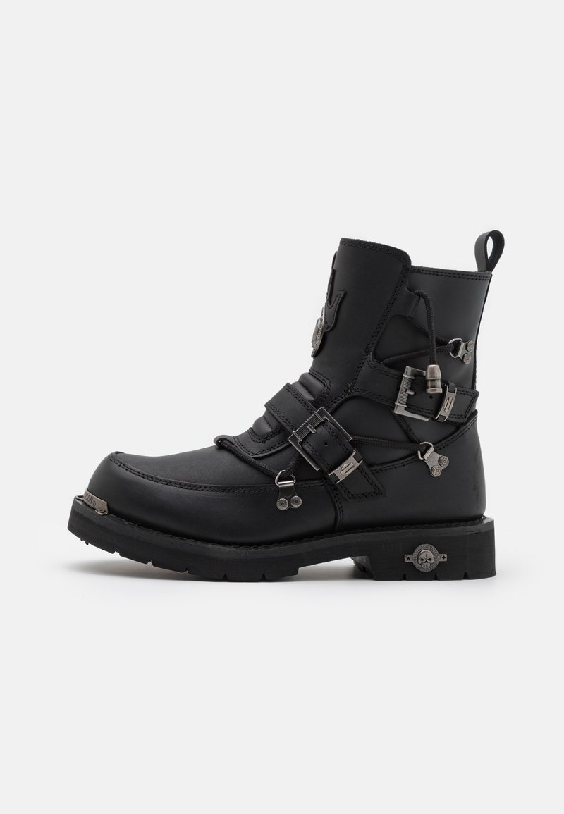 Botines de cuero negro con hardware metálico, múltiples correas, puntera redonda, superficie texturizada y una suela de goma gruesa con un acento decorativo.