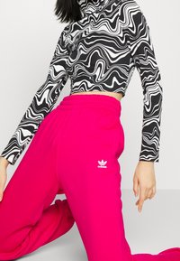 Černobílý top s vlnkovaným vzorem a dlouhým rukávem, který je kombinován s elastickými neonově růžovými tepláky s bílým logem Adidas.