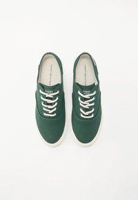 Grüne Leinensneaker mit weißen Gummisohlen, weißen Schnürsenkeln, runder Zehenpartie und einem auf derInnensohle gedruckten Logo.