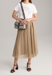 Camiseta blanca con un diseño gráfico, falda plisada beige, bolso negro decorado y sandalias negras de tacón alto con correas en el tobillo.