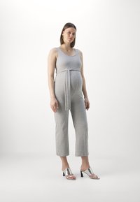 Grå graviditetsdress med tettsittende topp, brede cropped ben og belte med knyting i livet. Modellen har på seg metalliske høye sandaler.