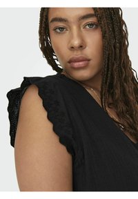 Crni top s v-neck dizajnom, teksturiranom tkaninom, ukrašenim čipkastim rukavima i glatkom završnom obradom. Vidljiva suptilna zlatna lančić ogrlica.