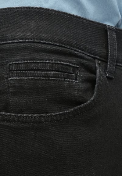 Μαύρο τζιν παντελόνι με πίσω τσέπη, με ραφές στο ίδιο χρώμα και λεία υφή. Ζώνη μέσης ορατή στο επάνω μέρος.