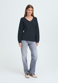 Mörkblå stickad tröja med v-ringning och ribbad textur, kombinerad med ljusgrå raka jeans och beigefärgade sneakers.