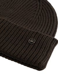 Căciulă tricotată maro cu țesătură verticală, având un tiv pliat și un mic logo metalic cusut pe lateral. Textură moale.