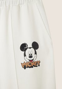 Los pantalones de chándal blancos presentan un gráfico impreso de Mickey Mouse, con orejas de lentejuelas negras y "MICKEY" en letras gruesas y marrones debajo.