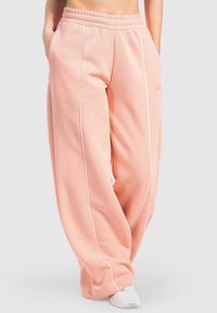 Pantalones de chándal ajustados sueltos de color rosa claro, fabricados con una tela suave, con ribetes blancos a lo largo de las costuras laterales y una cinturilla elástica.