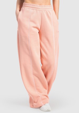 Lichtroze, loszittende joggingbroek van zachte stof, met witte bies langs de zijnaad en een elastische tailleband.