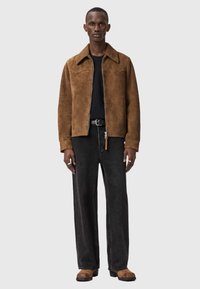 Ruskea mokkatakki kauluksella, yhdistettynä mustaan t-paitaan, väljiin mustiin farkkuihin ja ruskeisiin kenkiin. Asussa on yksinkertainen muotoilu.