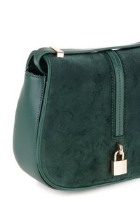 Borsa verde con finitura scamosciata, dettagli in pelle liscia, forma arrotondata e chiusura a lucchetto dorato sul lato.