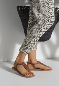 Ruske nahkakeeled nahkkingadega, tasasel põhjal, ja pahkluu rihmaga, koos musta ja valge mustriga pükstega ja kootud ostukotiga.