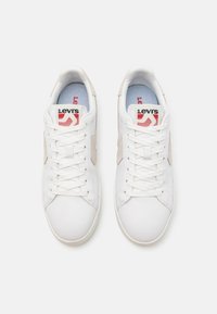 Białe skórzane sneakersy z beżowymi zamszowymi akcentami, okrągły czubek i płaskie białe sznurówki. Posiadają czerwono-czarną logo na języku.