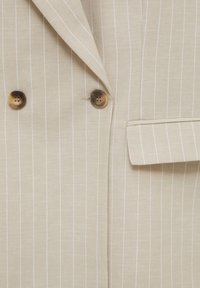 Blazer beige con rayas que presenta un cierre de doble botón, solapas con muesca y un bolsillo en el pecho, todo con una textura de tela suave.