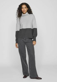 Suéter de cuello alto en bloque de colores gris y gris oscuro, con mangas largas, combinado con unos jeans oscuros de corte holgado. Textura de punto suave.
