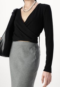 Svart omlottopp med långa ärmar kombinerad med en ribbad grå kjol. Outfiten har en slät textur och en lager-på-lager-design, kompletterad med en handväska.