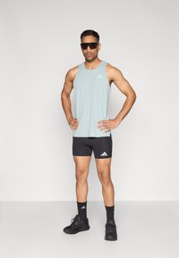 Šviesiai mėlynas rankovių neturintis marškinėlis, juodi sportiniai šortai, juodos kojinės ir sportbačiai. Ant marškinėlių ir šortų yra Adidas logotipas. Lygios audinio tekstūros.