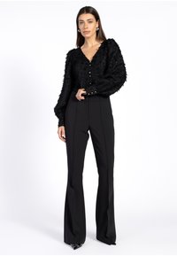 Zwarte gestructureerde cardigan met een V-hals en knoopsluiting, gecombineerd met hoge zwarte flared broek met een gladde, op maat gemaakte afwerking.