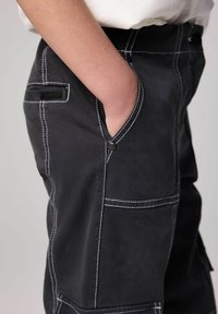 Mustat cargo-housut, joissa on valkoiset kontrastitikkaukset, sivutaskut ja rento istuvuus. Valmistettu kestävästä puuvillamateriaalista.