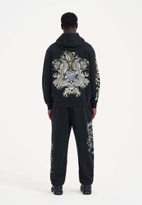 Svart hoodie och sweatpants-set med intrikata grafiska mönster på ryggen och benen, med djärva färger och detaljerade mönster.