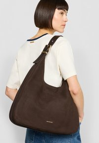 Bruine leren schoudertas met een gladde textuur en een gouden logo. Strak, afgerond ontwerp en brede schouderriem voor comfortabel dragen.