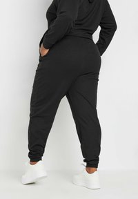 Svarta ribbade joggers med elastiska mudd, sidofickor och avslappnad passform. Matchat med vita sneakers, som visar upp en avslappnad design.