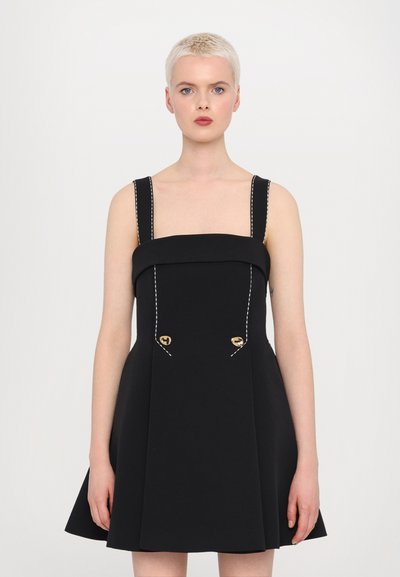 Sorte kjole med firkantet halsudskæring, brede stropper og en tætsiddende bodice. Har hvid syning og guldknapdetaljer på fronten. A-line silhuet.