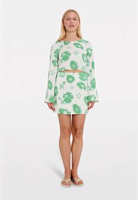 Haut court à motif floral vert avec des manches longues et jupe mini assortie, le tout en tissu doux et texturé.