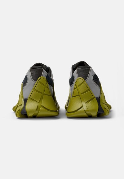 Calzature con una parte superiore grigia e nera, caratterizzate da pannelli in rete e suole in gomma verde oliva, che presentano un design del tallone scolpito e accenti testurizzati.