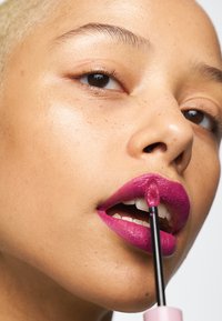 Glansig, ljus fuchsiahudfärg applicerad med en svart applikator. Modellen har slät, ljus hy med en närbild på läpparna och ögonen.