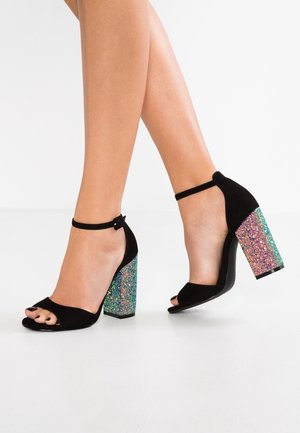 Black suede open-toe high heels with a chunky multi-colored glitter heel. Features an ankle strap and a smooth black sole.