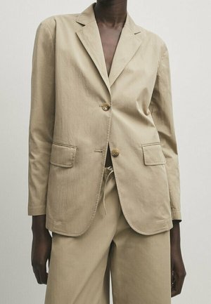 Veste beige en tissu léger, à un bouton avec deux poches avant, à revers cranté et fermeture à bouton. Texture lisse.