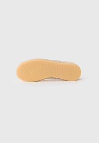 Semelle de chaussure avec un motif en nid d'abeille, fabriquée en caoutchouc de couleur miel, présentant une finition lisse et sans logos ni détails visibles.