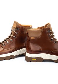Bottes de randonnée en cuir marron avec des accents beiges, œillets en métal, lacets texturés, col rembourré et semelle Vibram® pour une meilleure traction.