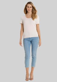 Lichtroze shirt met korte mouwen, gecombineerd met lichtblauwe capri-jeans met een decoratieve kraalrand langs de zijkanten. Transparante sandalen met hakken.