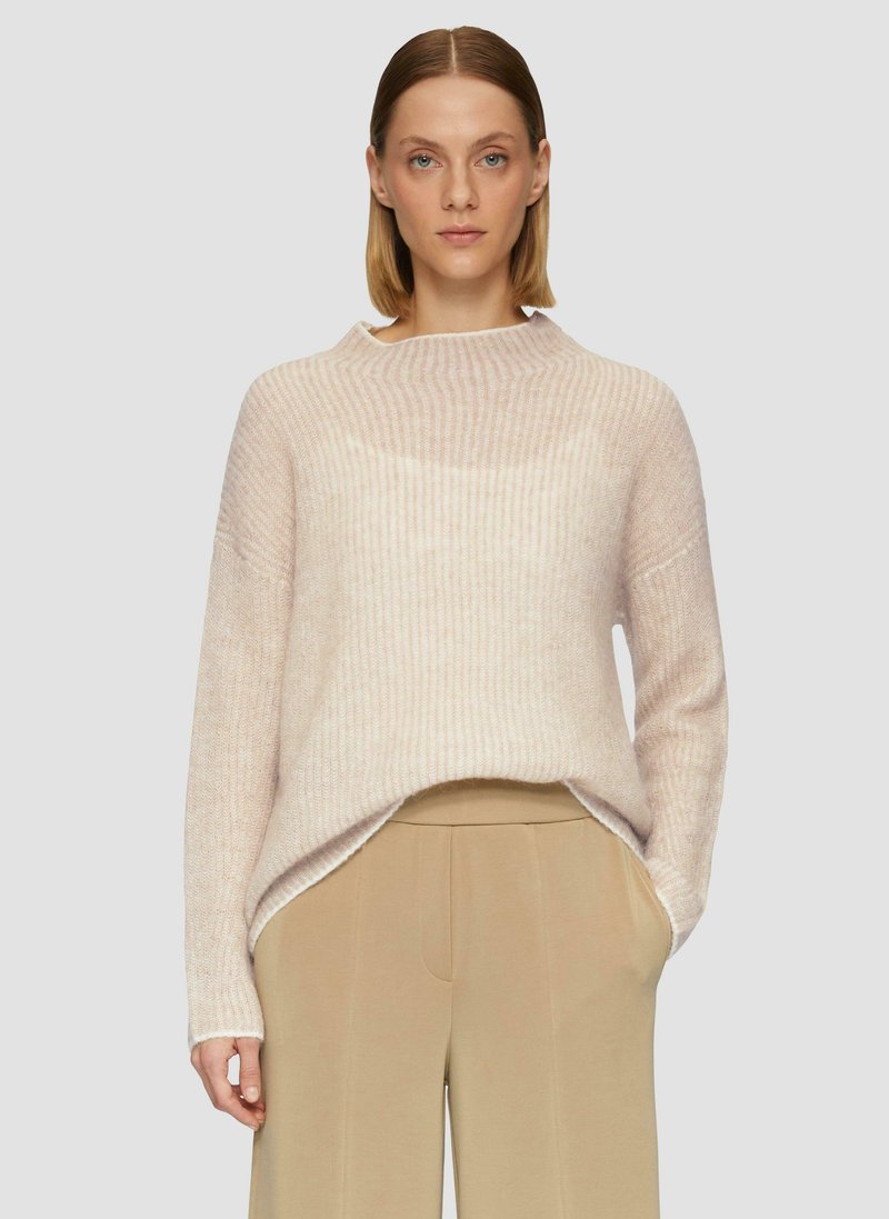 Hellrosa gestrickter Pullover mit hohem Kragen, gerippter Textur und leicht oversized Passform, kombiniert mit beigen, weit geschnittenen Hosen.