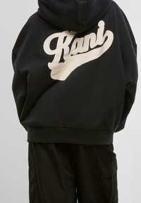 Felpa nera con cappuccio caratterizzata da una grande scritta in cremoso "Kani" sul retro, con vestibilità rilassata e orlo a costine. Abbinata a pantaloni cargo neri.