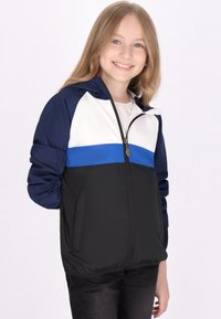 Ungdomsjakke med lynlås foran, i farveblokeret design i navy, hvid og sort, med en blå vandret stribe og sidelommer.