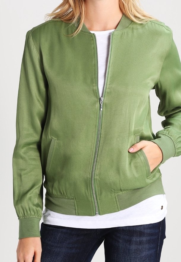 Veste bomber verte en tissu lisse, dotée d'une fermeture éclair à l'avant, de deux poches latérales et de poignets élastiques. Portée sur une chemise blanche.