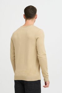Suéter de manga larga beige, diseño ajustado, con puños y dobladillo acanalados, fabricado en un tejido de punto suave, con cuello redondo y detalles mínimos.