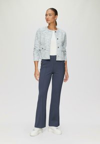 Geweven lichtblauwe jas met gouden knopen, witte top en marineblauwe wijde broek. Outfit afgerond met witte chunky sneakers.