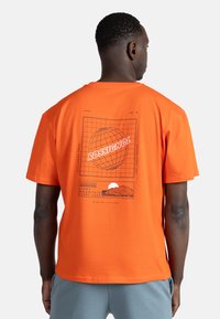 Orange bomulds t-shirt med et grafisk design med en globe, bjerg og tekst på ryggen. Korte ærmer og rund hals.