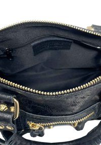 Interior de un bolso de mano de cuero negro que presenta un cierre de oro, textura suave, un parche de velcro y un pequeño bolsillo con cremallera en un lado.