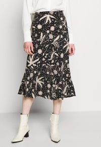 Mustat midi-hameet, joissa on beige kukkakuvio ja tähtikuvio, avara helma ja sileä rakenne, yhdistettynä kermanvärisiin nilkkasaappaisiin.
