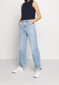 Marinblå ärmlös polo med krage, kombinerad med ljusblå högmidjade raka jeans och vita sportskor.