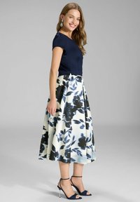 Ein marineblaues Oberteil mit kurzen Ärmeln, kombiniert mit einem langem, geblümtem Rock in Blau und Weiß, akzentuiert durch marineblaue Riemchenabsätze.