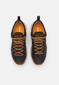 Zapatillas deportivas negras con parte superior de malla, cordones naranjas y detalles marrones. Presentan una lengüeta acolchada, punta redonda y suela de goma.