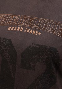 Czarny bawełniany t-shirt z napisem "TRUE RELIGION BRAND JEANS" w pomarańczowym haftem, z dużą ciemną cyfrą "2" wyraźnie nadrukowaną.