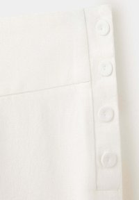 Gros plan d’un tissu blanc avec quatre boutons ronds blancs alignés verticalement le long du bord d’une couture de vêtement.