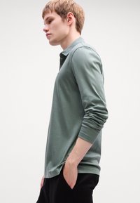 Green long-sleeve polo shirt made of soft fabric, featuring a collared neckline and slim fit, with rolled cuffs and a relaxed silhouette.